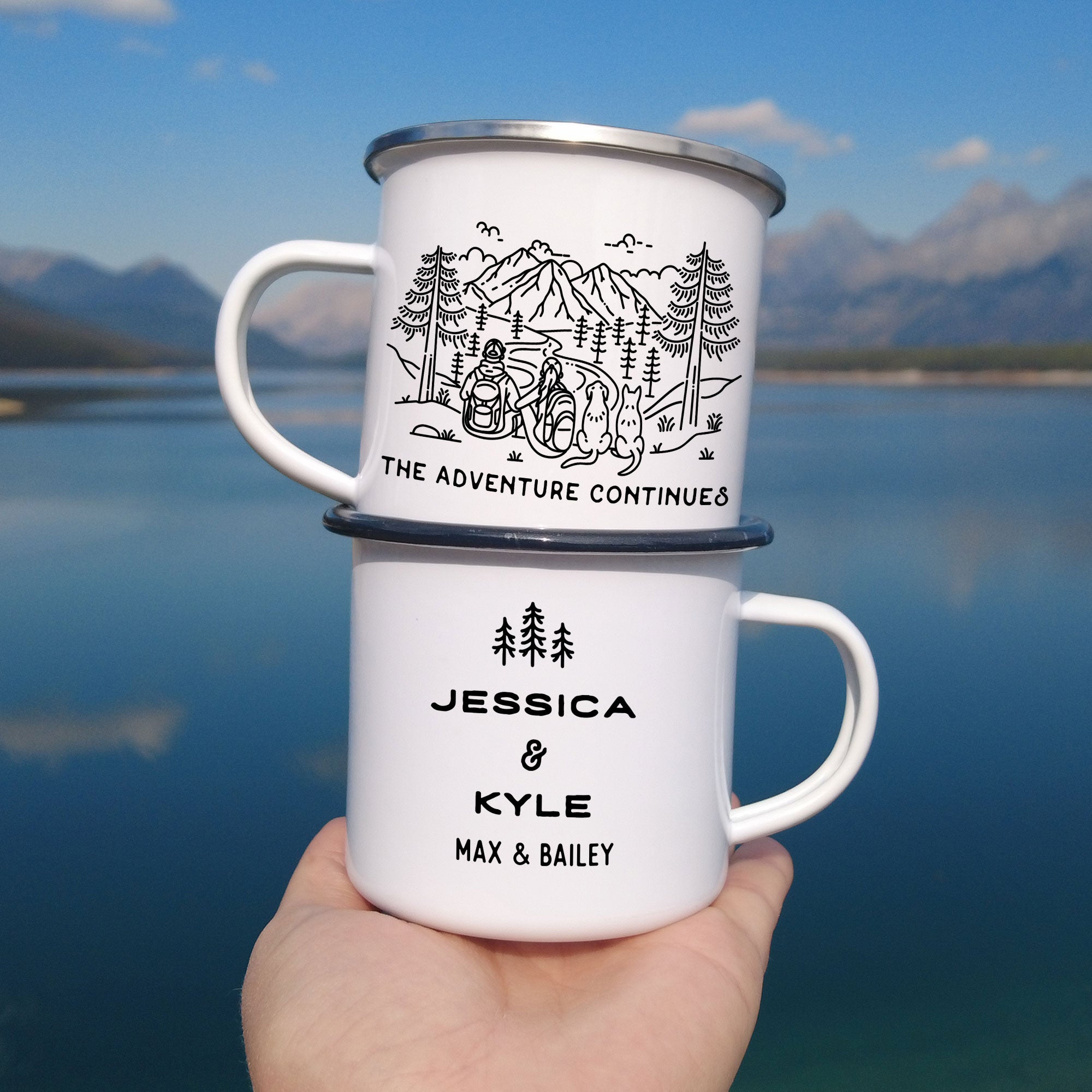 Stacked black & silver rimmed enamel mugs. Features original hand drawn line artwork of mountain hiking couple & two dogs (1 floppy eared & 1 pointy eared). Text on front of mug shows 'The Adventure Continues'. Design on back of mug is of three line art trees and the text 'Jessica & Kyle, Max & Bailey.'