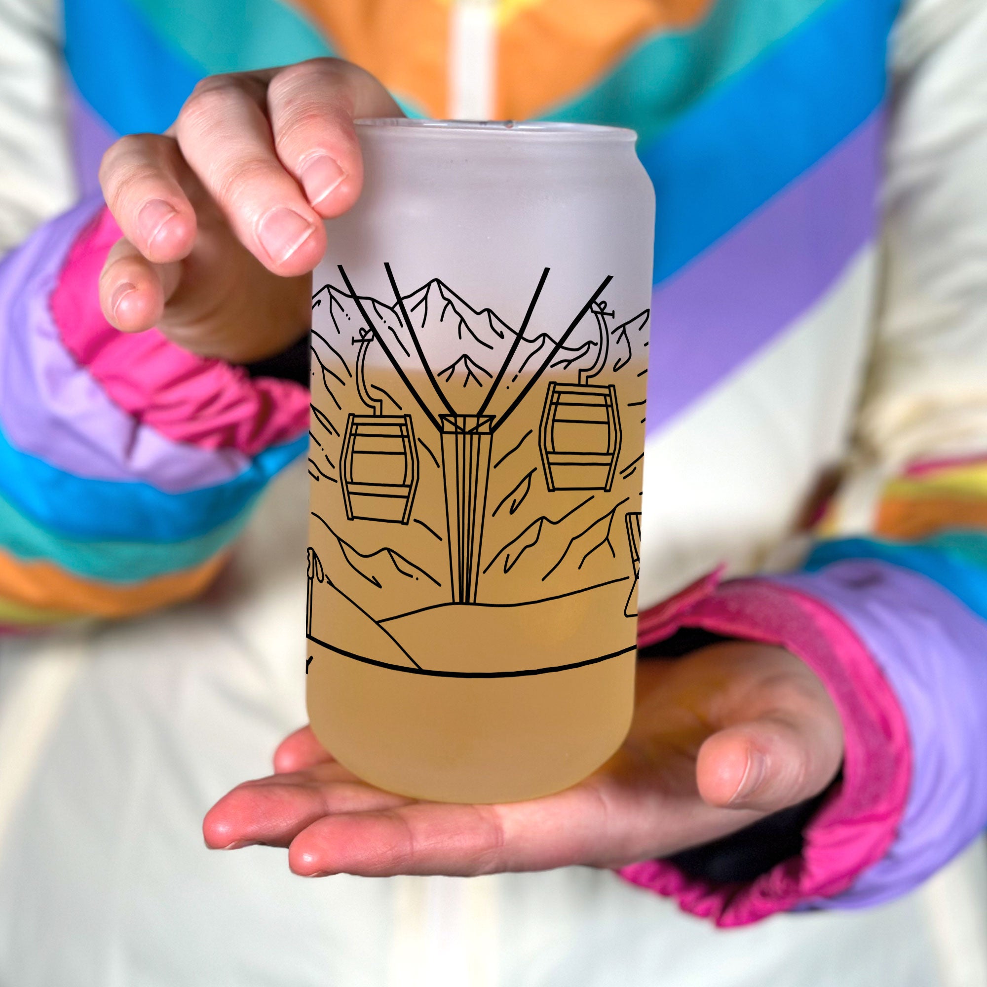 Hand holiding frosted glass tumbler. Shows middle ski couple line art design of ski chair lift.