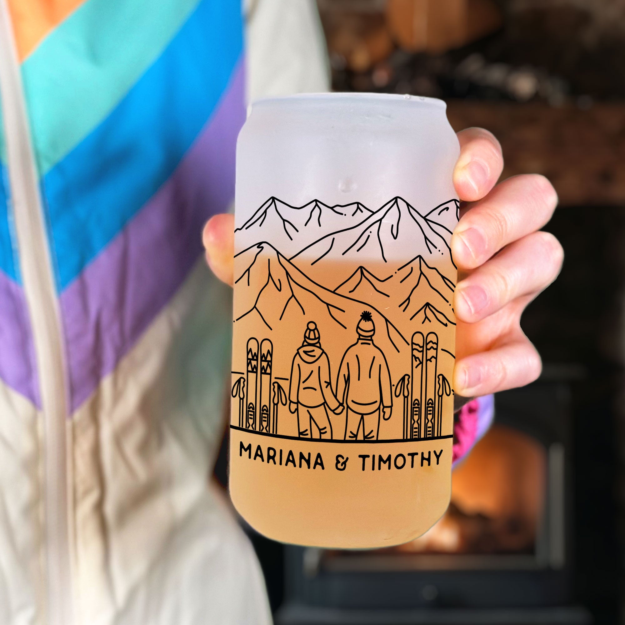 Hand holiding frosted glass tumbler. Shows front ski couple line art design. Text Mariana & Timothy on the bottom under the couple.