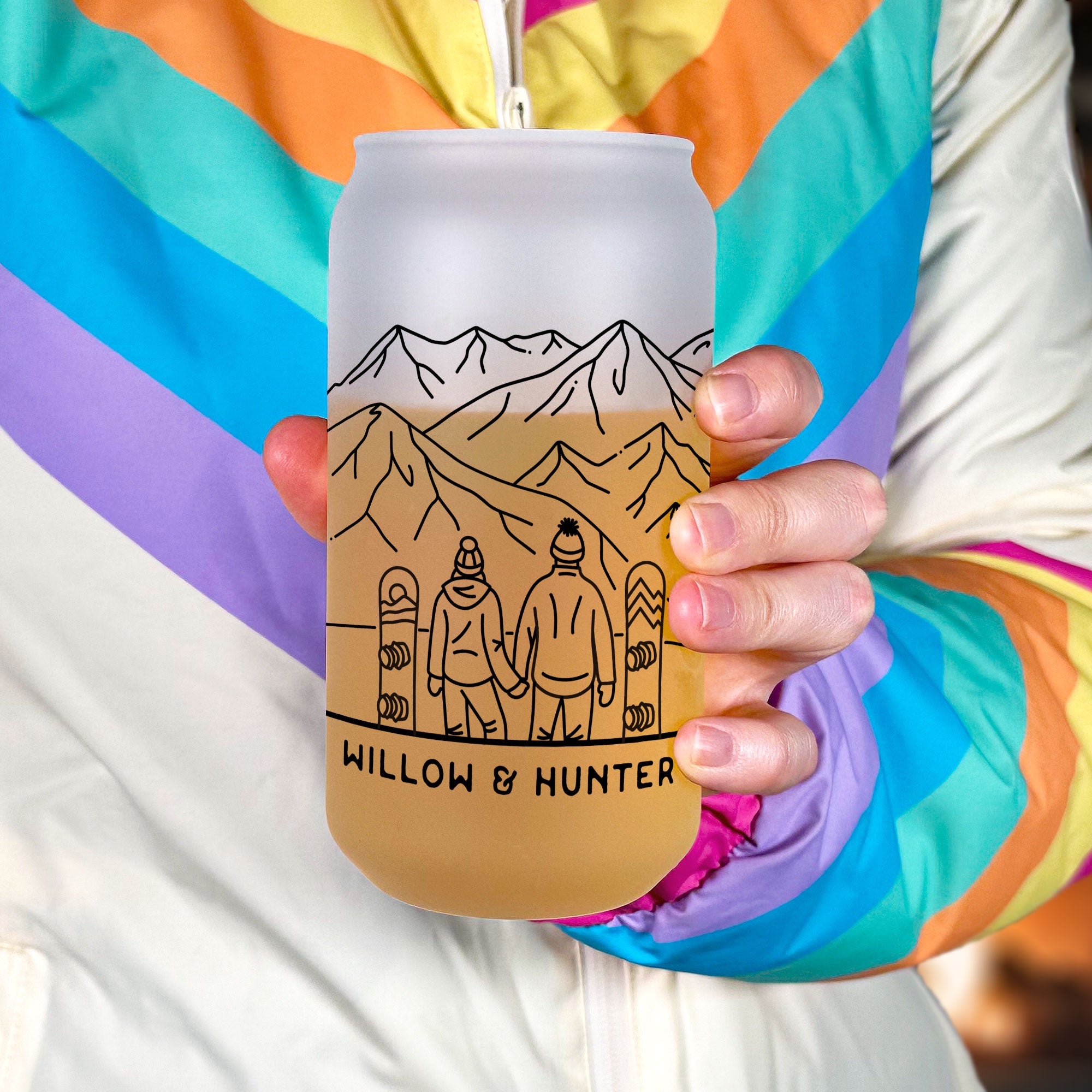 Hand holiding frosted glass tumbler. Shows front snowboarding couple line art design. Text Willow & Hunter on the bottom under the couple.