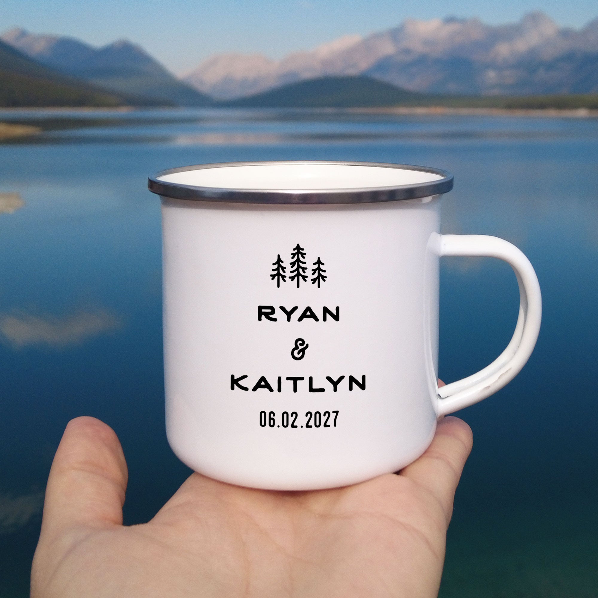 Close-up of hand holding single silver rimmed enamel mug. Photo references the back (or right side) of the enamel mug design. The back has 3 Line Art Trees and the text 'Ryan & Kaitlyn 06.02.2027'